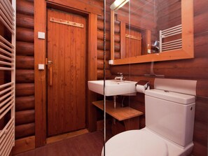 Un bagno in stile baita con pareti in legno, una porta di legno, un lavandino bianco, un water e uno specchio sopra il lavandino.