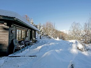 Una baita di legno con un portico coperto, circondata da alberi innevati e un cielo sereno.
