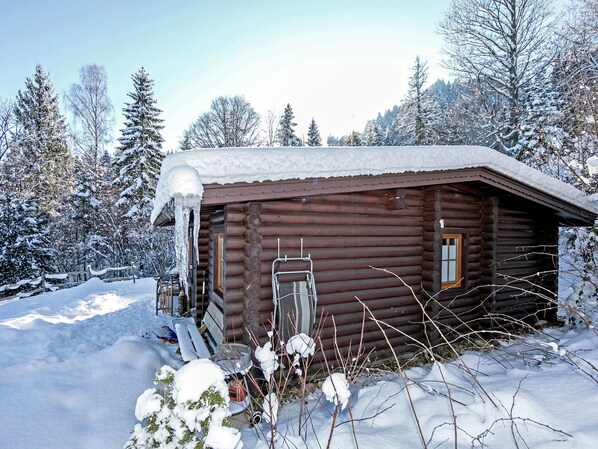 Une cabane en rondins dont le toit est recouvert de neige, entourée d’arbres chargés de neige.