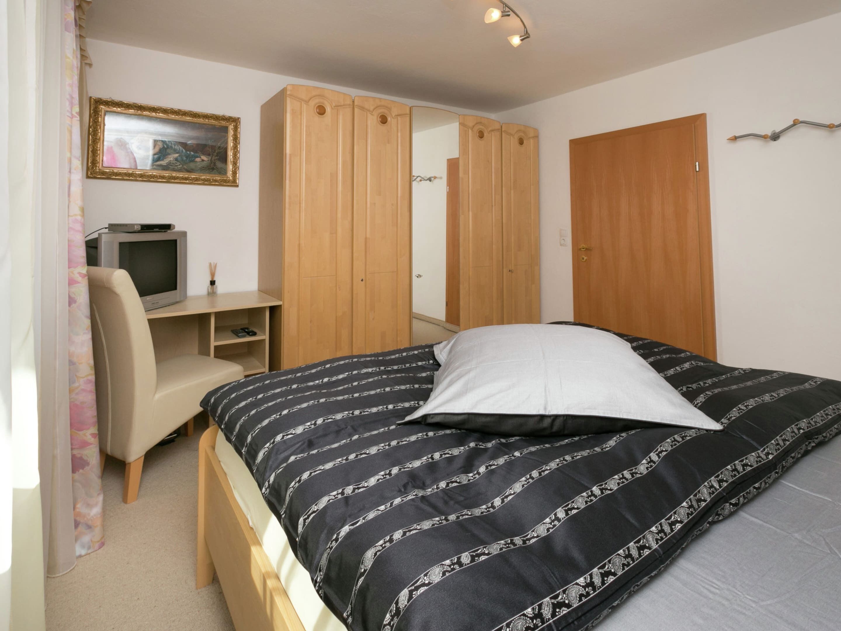 A bedroom with a bed, a desk, a chair, a wardrobe, and a television.