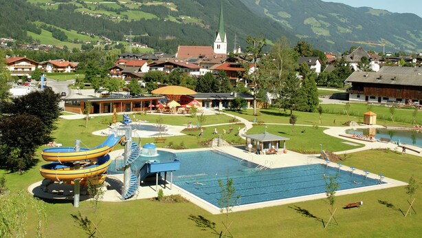 Un complexe hôtelier doté d’une grande piscine, de toboggans aquatiques et offrant une vue sur une ville, avec une église en arrière-plan.