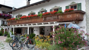 Un immeuble doté d’un balcon orné de fleurs rouges, d’un porte-vélos et d’une enseigne indiquant la présence d’un bar, d’un café et d’un restaurant de pizzas.