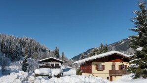 Een met sneeuw bedekte berglodge met twee hoofdgebouwen, omgeven door sneeuwzware bomen en bergen.
