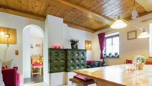 Een gezellige kamer met een houten plafond, een eettafel met stoelen, een bankje en een groen kastje met ronde patronen.