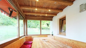 A wooden dining table with benches, large windows, and a view of greenery outside.