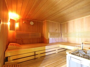 A sauna room with wooden benches and benches, a wall-mounted heater, and a clock. - Vintage Apartment With Sauna in Hopfgarten (Hopfgarten im Brixental)