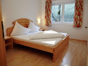 Un lit en bois avec une literie blanche, dans une pièce dotée d’une fenêtre et de rideaux.