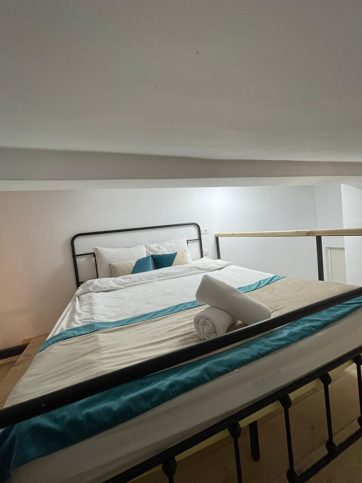 Un lit simple avec un cadre en métal, une literie blanche et des touches de couleur turquoise.