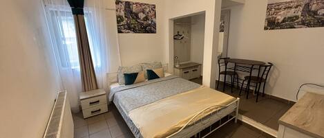 A bedroom with a bed, a desk, a chair, a radiator, and a mirror.