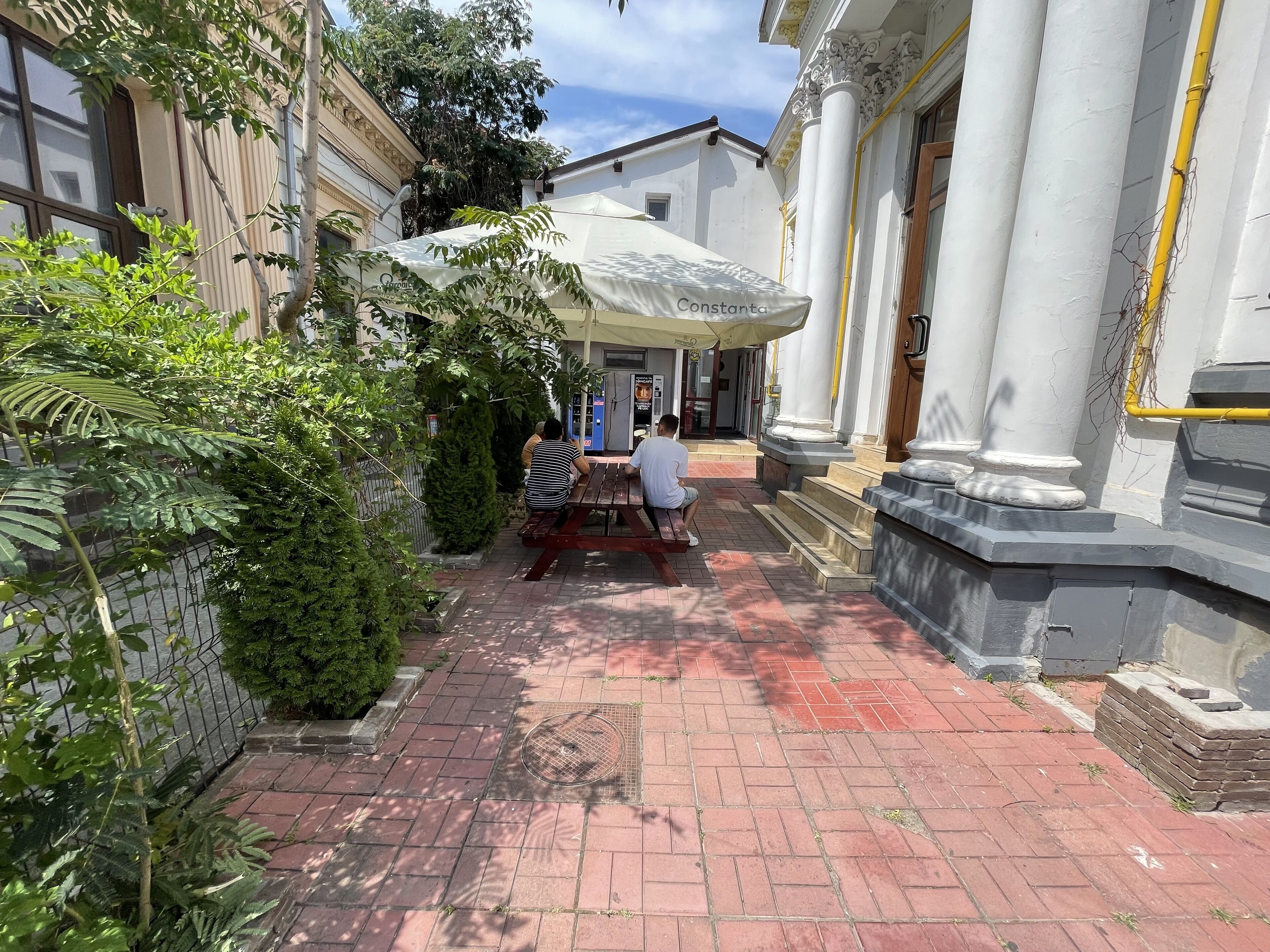 Un cortile con un vialetto in mattoni, un edificio bianco con colonne e un’area salotto coperta.