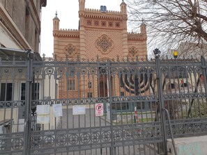 Una entrada protegida por un portón con cercado de hierro decorativo, un edificio con detalles arquitectónicos intrincados y una bandera.