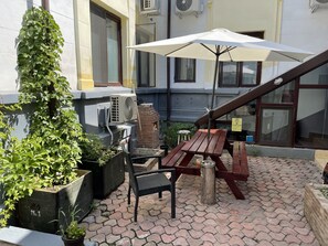 Un patio al aire libre con una mesa y sillas de madera, un paraguas blanco y plantas en macetas.