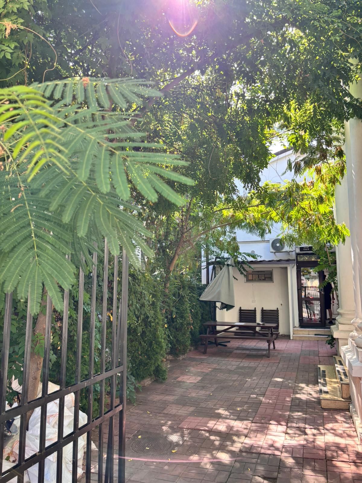 A paved pathway leading to a building with a covered seating area and a bench.