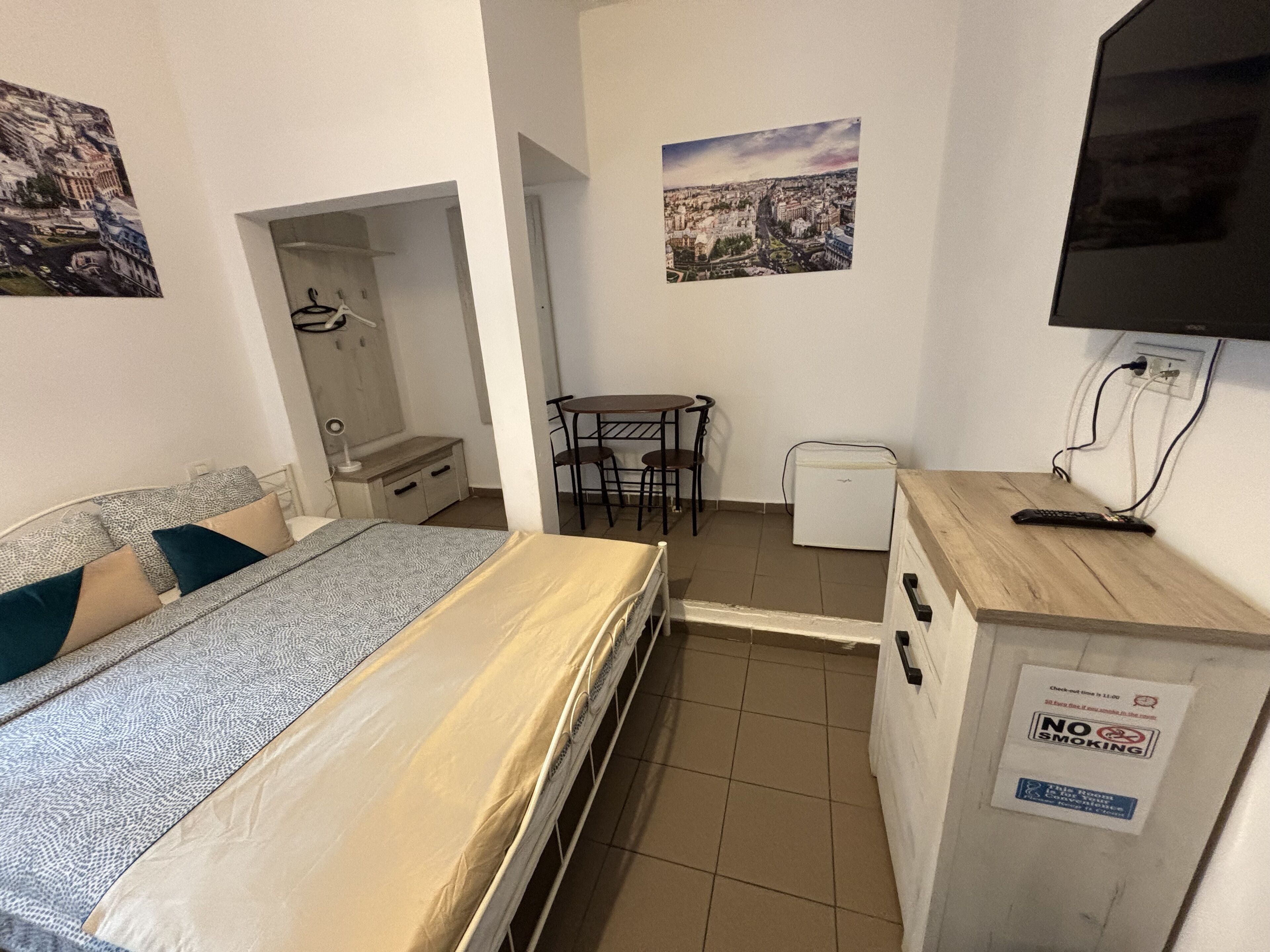 Una habitación de hotel compacta con una cama, un escritorio pequeño, un refrigerador y un televisor.