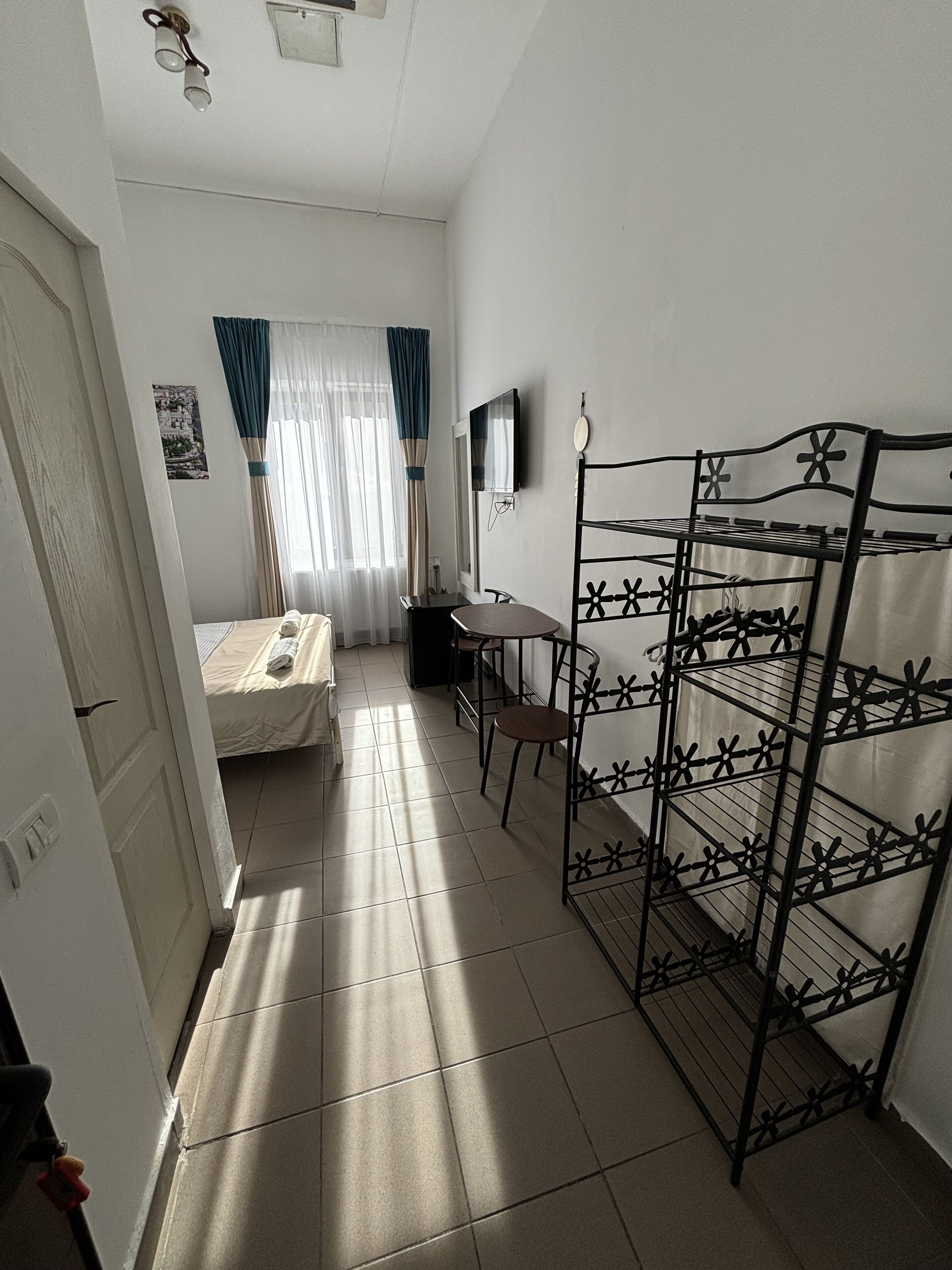 Une petite pièce comprenant un lit, un bureau, une chaise et un étagère en métal.