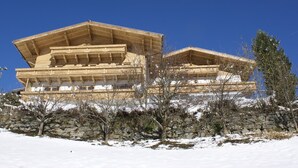 A large wooden building with multiple levels and a sloped roof, surrounded by snow and trees.