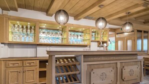 A wooden bar area with glass shelves displaying bottles and glasses, wooden cabinets, and pendant lights.