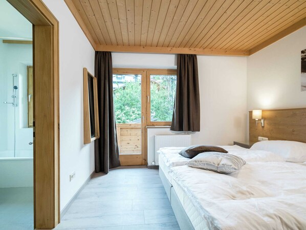 A bedroom with a wooden ceiling, a large window with curtains, a bed with pillows, and a wall-mounted lamp. - Large Luxury Chalet near Ski Area Zillerarena Königsleiten (Wald im Pinzgau)