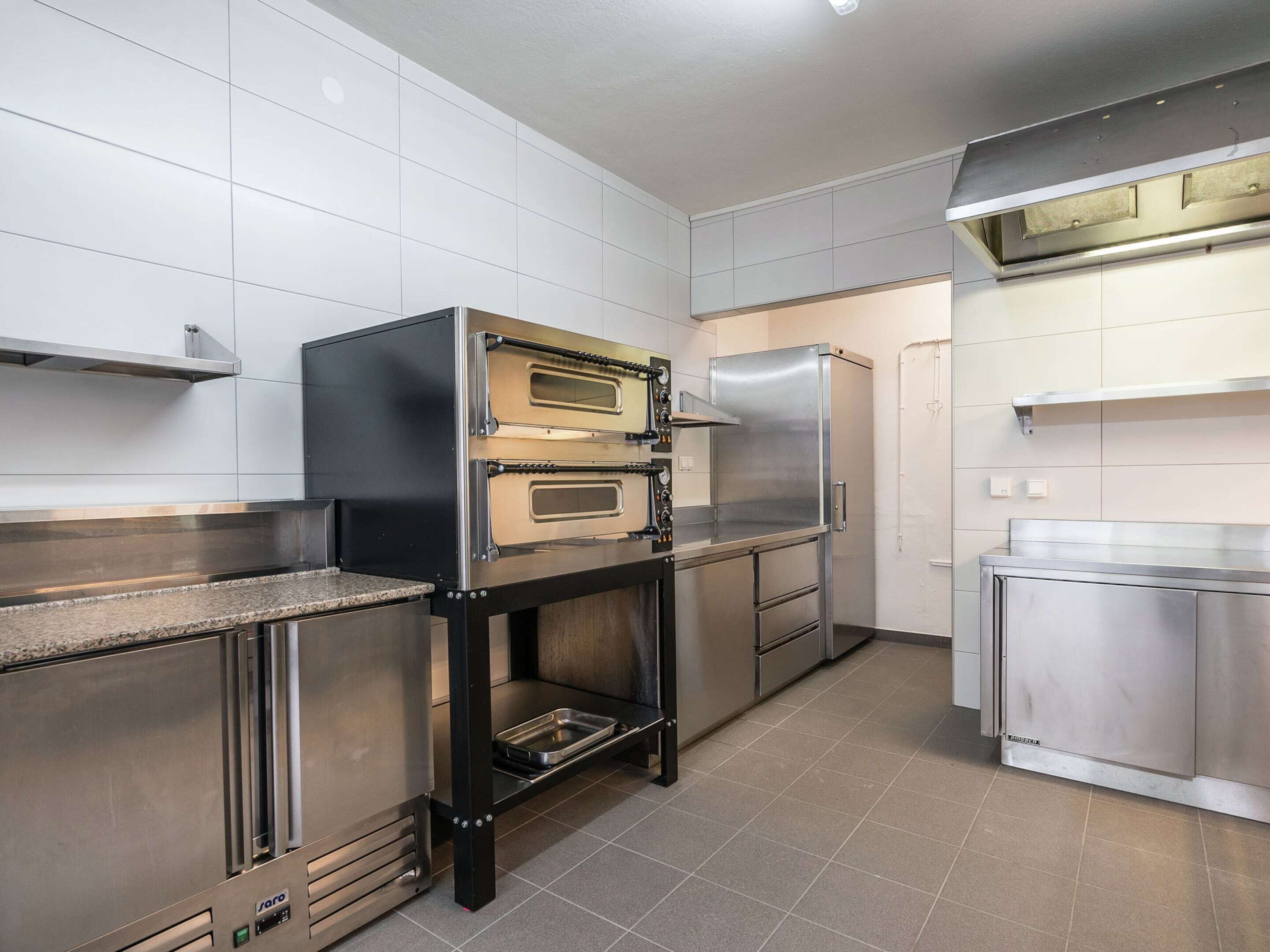 Uma cozinha comercial equipada com eletrodomésticos de aço inoxidável, incluindo forno duplo e geladeira.