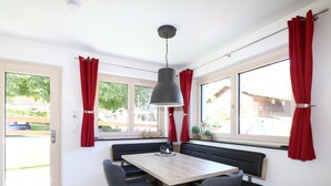 Una habitación moderna con una mesa de comedor de madera, dos sillas grises, un banco negro y una lámpara colgante.