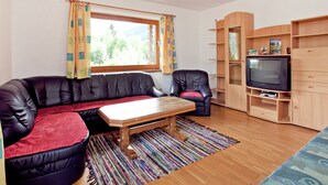 Ein gemütliches Wohnzimmer mit einer Ledersofa, einem Holztisch, einem Fernseher und einem Bücherregal.