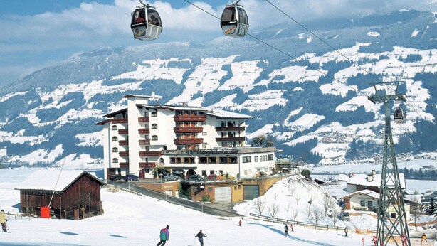 Ein Hotel mit mehreren Etagen, Skipfächern und einem verschneiten Berg im Hintergrund.