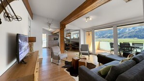 A spacious living room with a large TV, a sofa, and a dining area with a view of mountains. - Spacious Apartment in Piesendorf near Ski Area (Piesendorf)