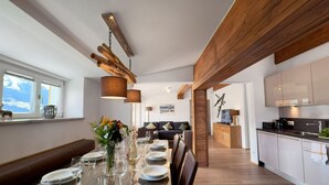 A modern kitchen with wooden beams, a dining area with a wooden table set for four, and a view of the mountains through the window. - Spacious Apartment in Piesendorf near Ski Area (Piesendorf)