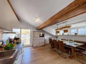 A modern kitchen with wooden beams, a dining area with a table set for four, and a view of the outdoors through large windows. - Spacious Apartment in Piesendorf near Ski Area (Piesendorf)
