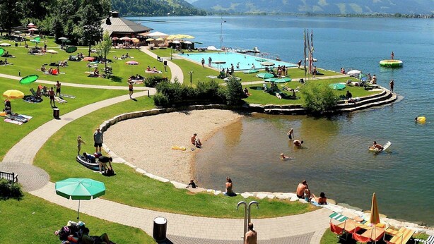 A lakeside resort with a swimming pool, sun loungers, and a grassy area with umbrellas. - Spacious Apartment in Piesendorf near Ski Area (Piesendorf)