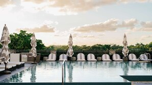 Un espace aménagé au bord de la piscine, avec des chaises longues et des parasols, un ciel dégagé et une vue sur les arbres en arrière-plan.