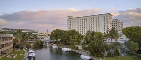 A marina with several boats docked, surrounded by lush greenery and a large hotel building in the background.