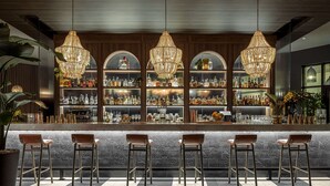 Un espace bar doté d’un long comptoir, de nombreux tabourets et d’un lustre décoratif.