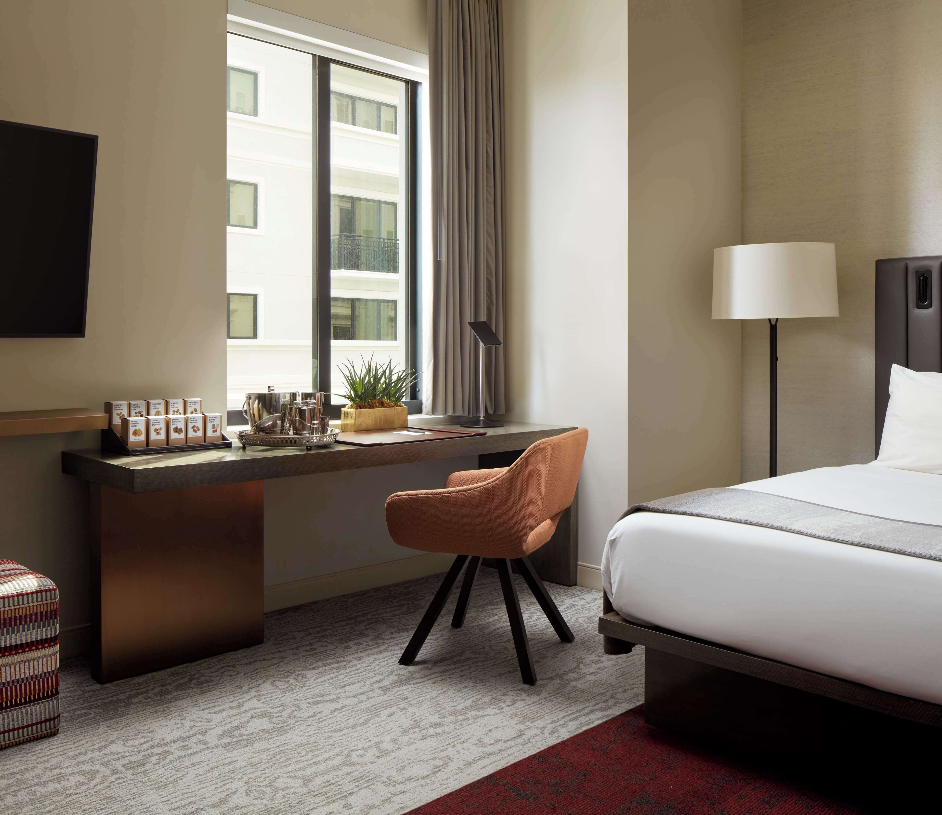 A hotel room with a bed, desk, chair, and a small table with amenities.