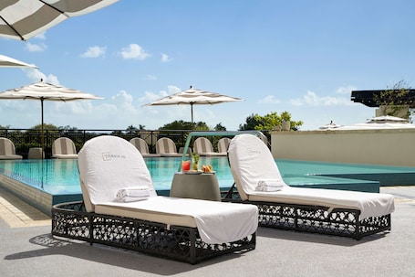 Una piscina al aire libre, sombrillas, sillones reclinables de piscina