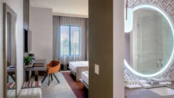 A hotel room with a bed, a desk, a chair, a small table, and a large mirror.