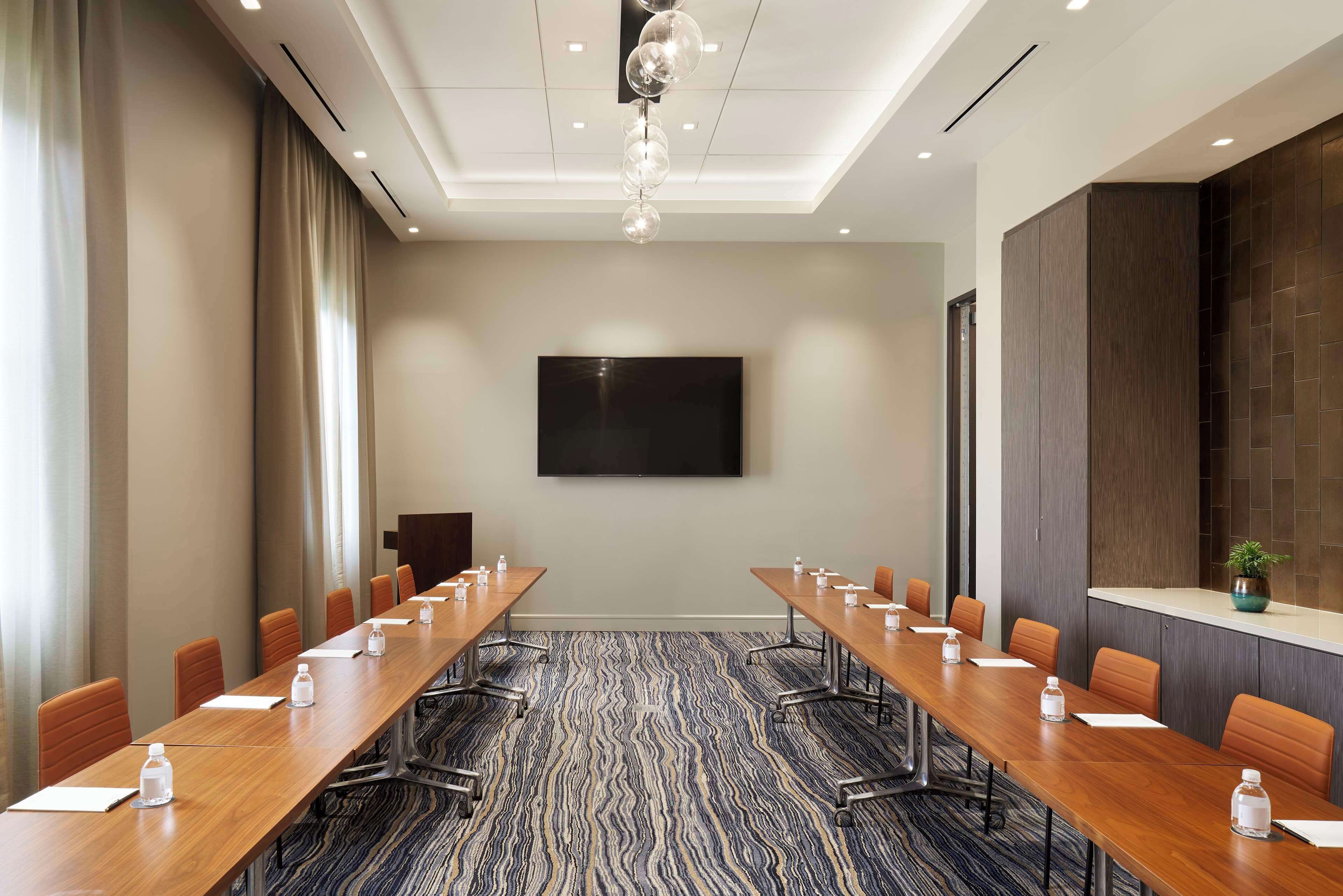 A conference room with a long table, chairs, a flat-screen TV, and a patterned carpet.