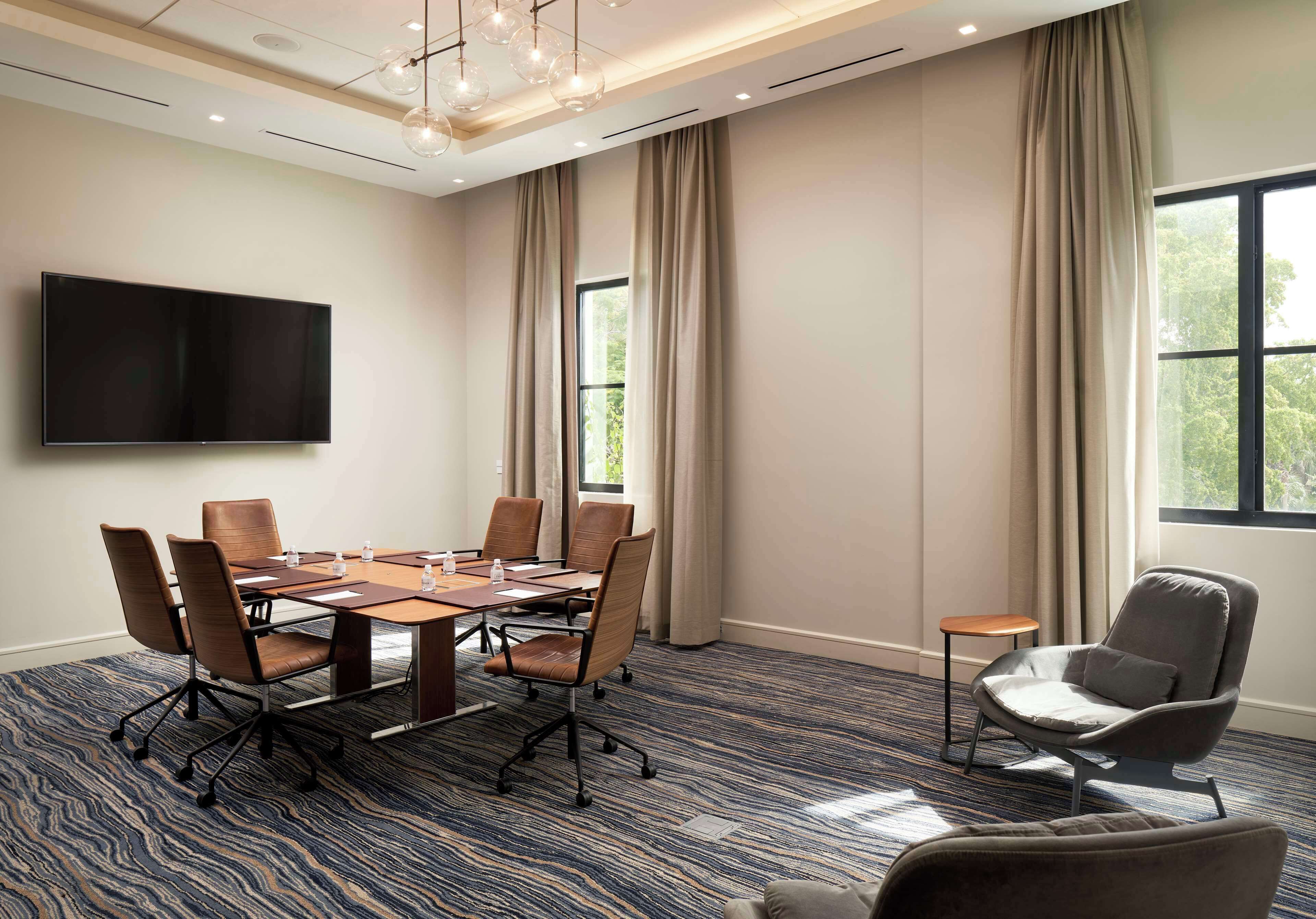 A conference room with a large table, chairs, a TV, and a window with curtains.