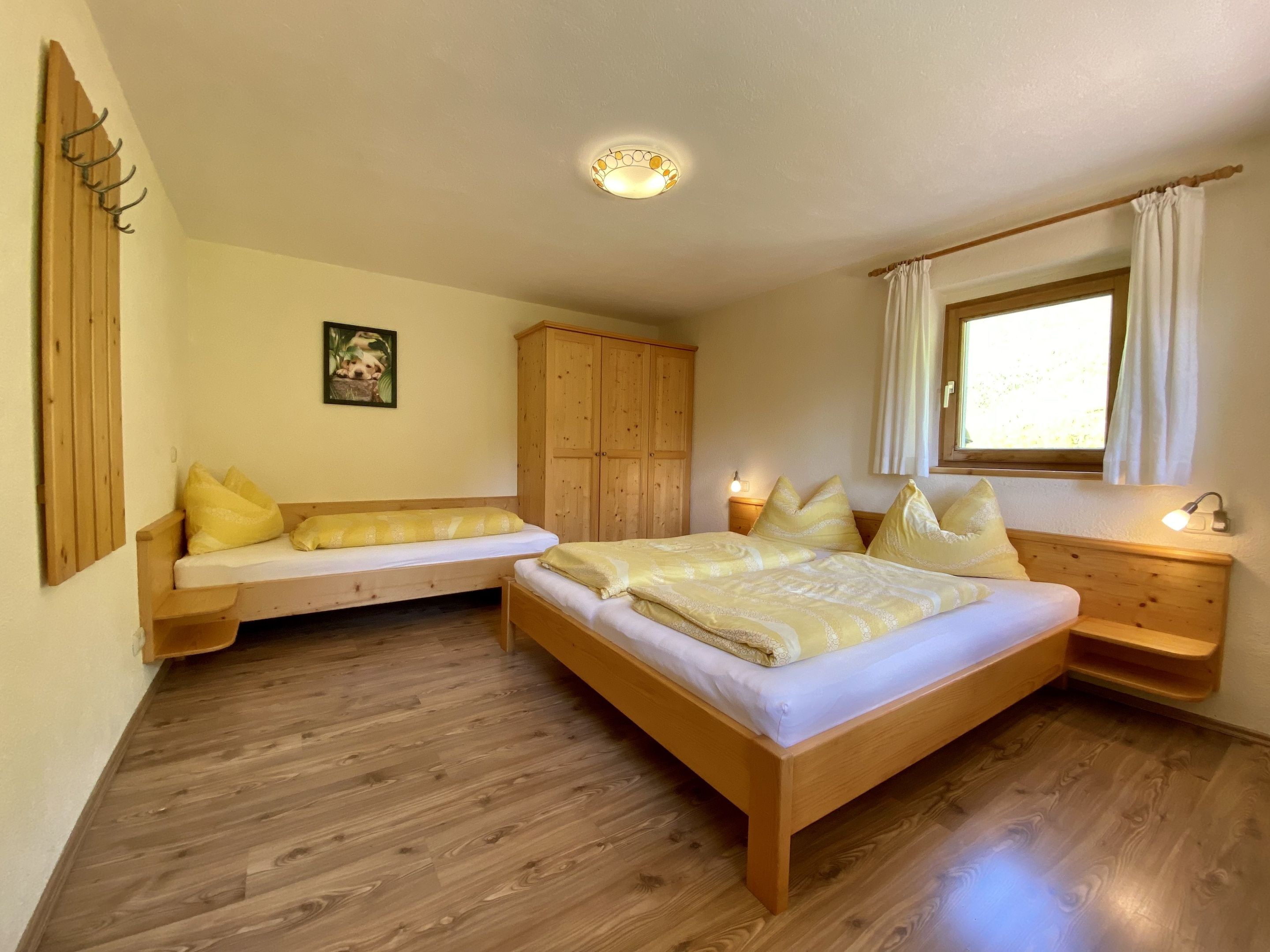 Une chambre à coucher avec un lit en bois, un banc en bois, une armoire, une table de chevet et une fenêtre avec des rideaux.