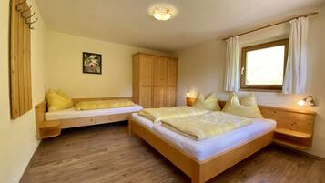 Une chambre à coucher avec un lit en bois, un banc en bois, une armoire, une table de chevet et une fenêtre avec des rideaux.