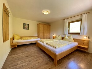 A bedroom with a wooden bed, a wooden bench, a wardrobe, a bedside table, and a window with curtains.
