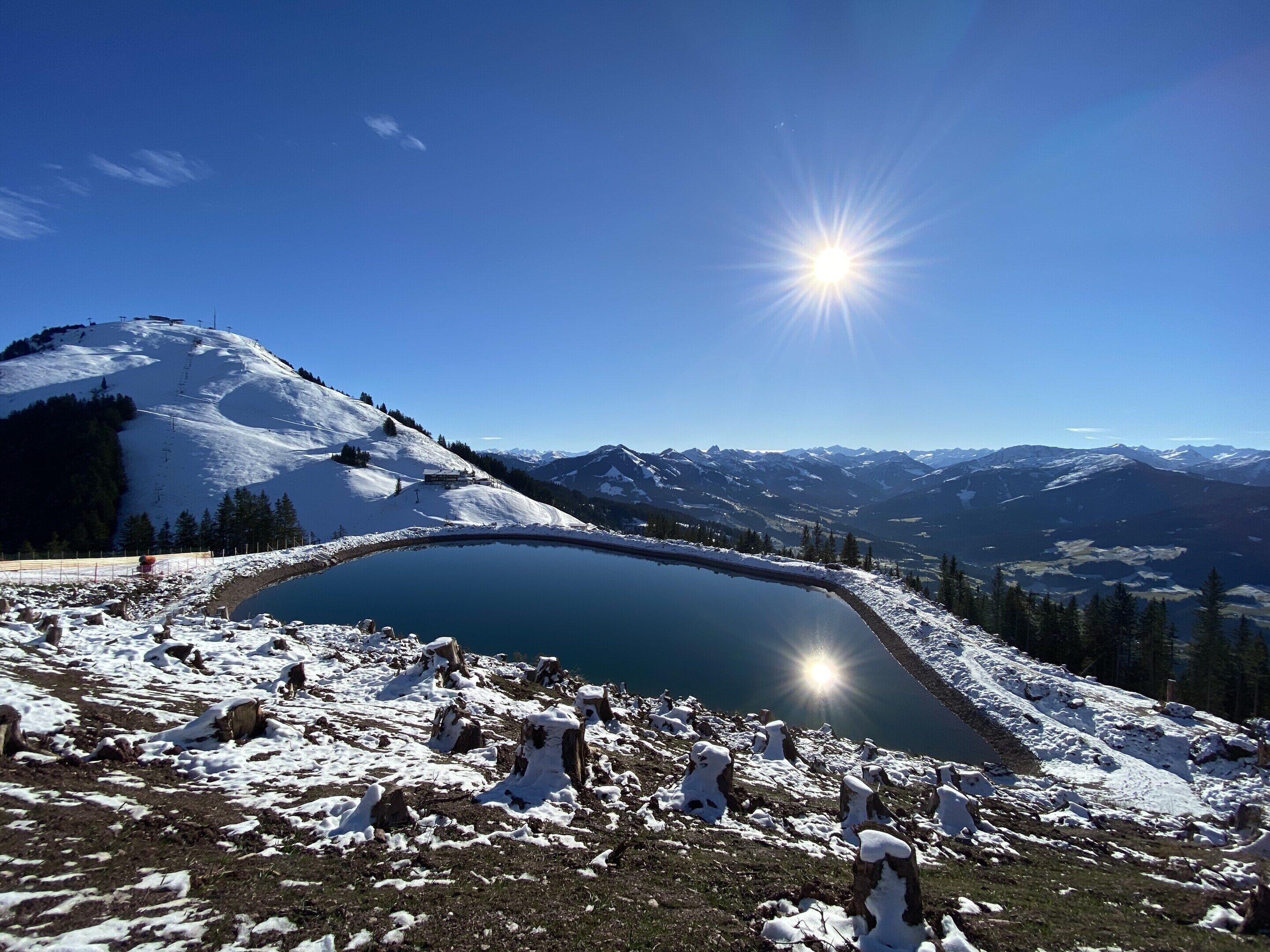 A snow-covered landscape with a lake, mountains in the background, and a clear sky.