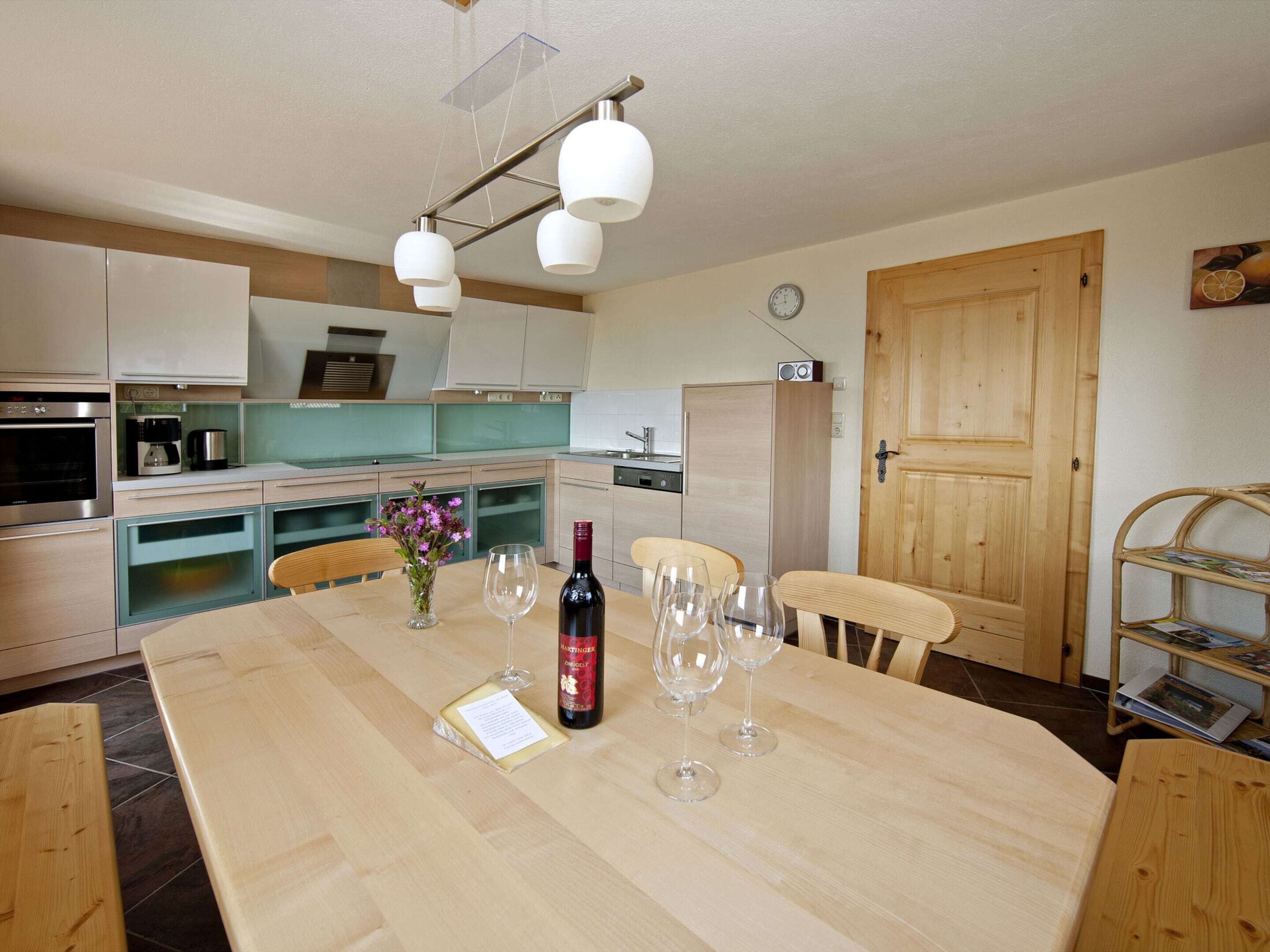 Una cocina moderna con electrodomésticos de acero inoxidable, una mesa de comedor de madera y copas de vino, y una puerta de madera.