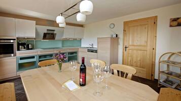 Una cocina moderna con electrodomésticos de acero inoxidable, una mesa de comedor de madera y copas de vino, y una puerta de madera.