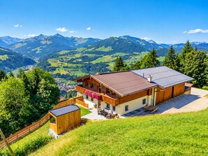 A chalet with a wooden deck, a small wooden structure, and a view of mountains and valleys.