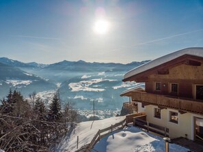 A wooden chalet with a balcony, surrounded by snow-covered mountains and a valley.