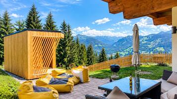 Une terrasse en bois avec mobilier d’extérieur, un barbecue et une vue sur les montagnes.