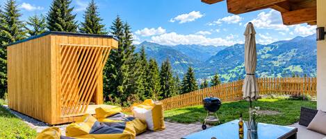 Une terrasse en bois avec mobilier d’extérieur, un barbecue et une vue sur les montagnes.
