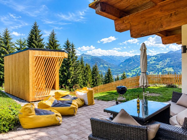 A wooden deck with outdoor furniture, a barbecue grill, and a view of mountains.