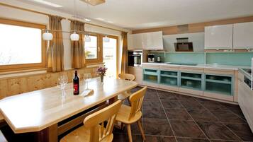 A modern kitchen with wooden cabinetry, a dining table with chairs, and a view of the outside through large windows.